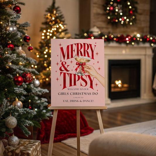 Pink Merry & Tipsy Christmas party welcome sign displayed on a wooden easel